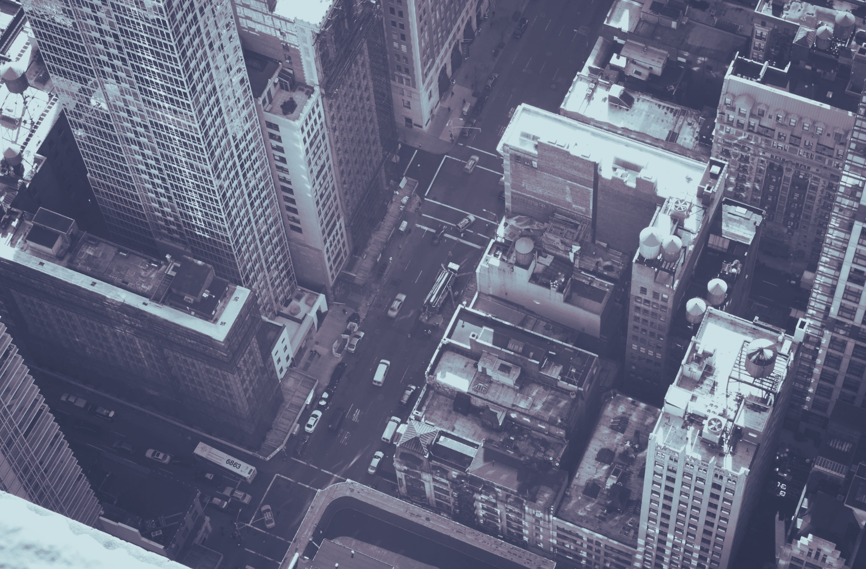 Black and white image from aeriel view of downtown city area with tall skyscrapers and cars in the street.